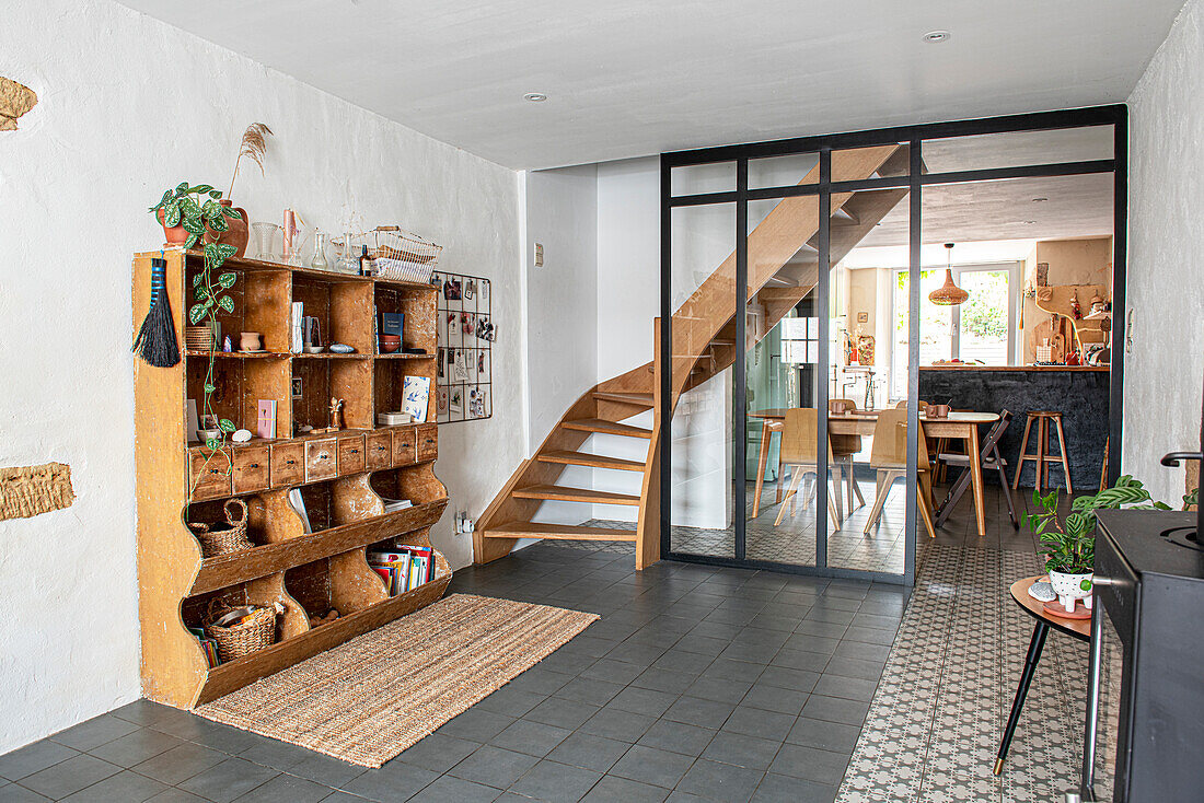 Living room with wooden staircase, open vintage wooden cupboard and tiled floor