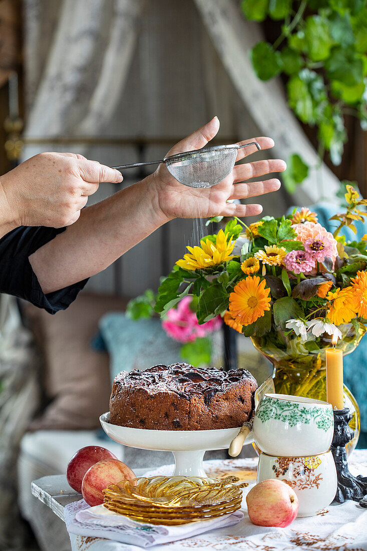 Kuchen wird mit Puderzucker bestäubt, bunter Blumenstrauß auf gedecktem Tisch