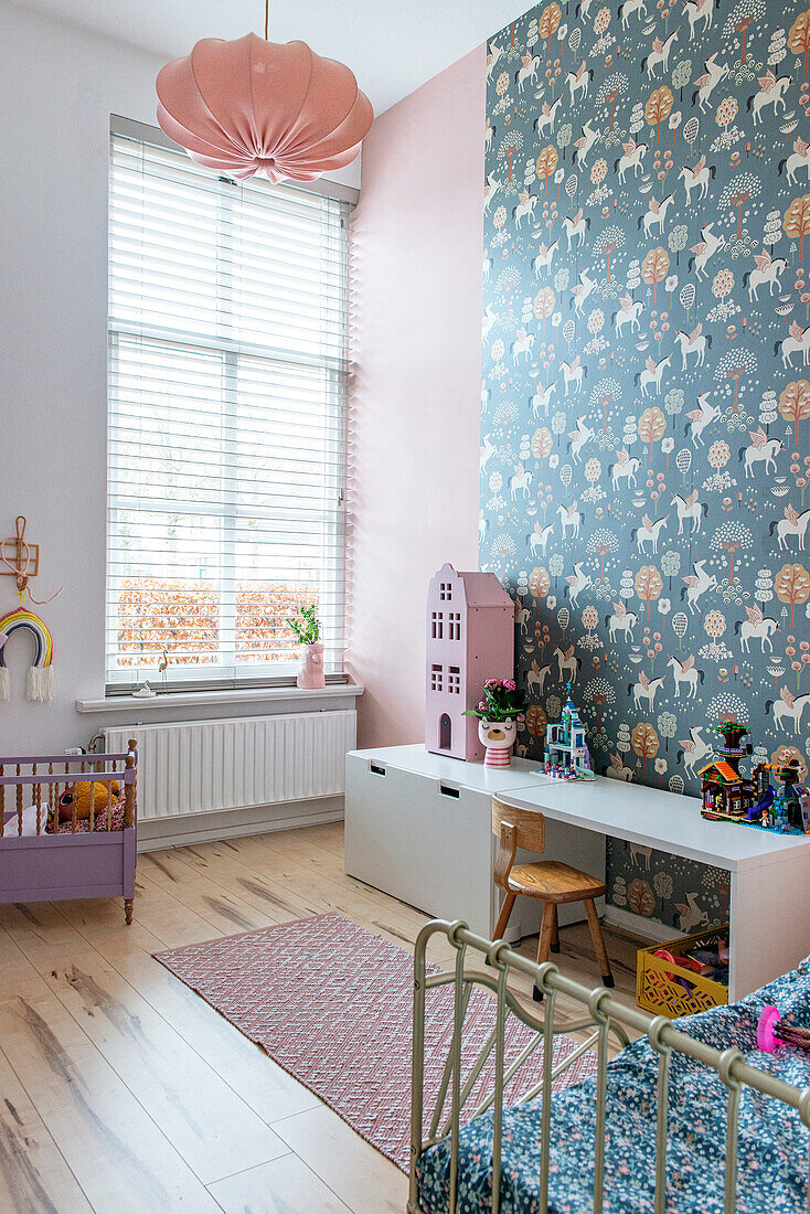 Kinderzimmer mit floraler Tapete, rosa Wandfarbe und pastellfarbenen Accessoires