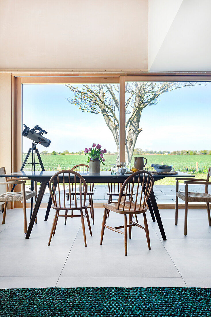 Essbereich mit Holzstühlen und Teleskop vor Panoramafenster mit Landschaftsblick