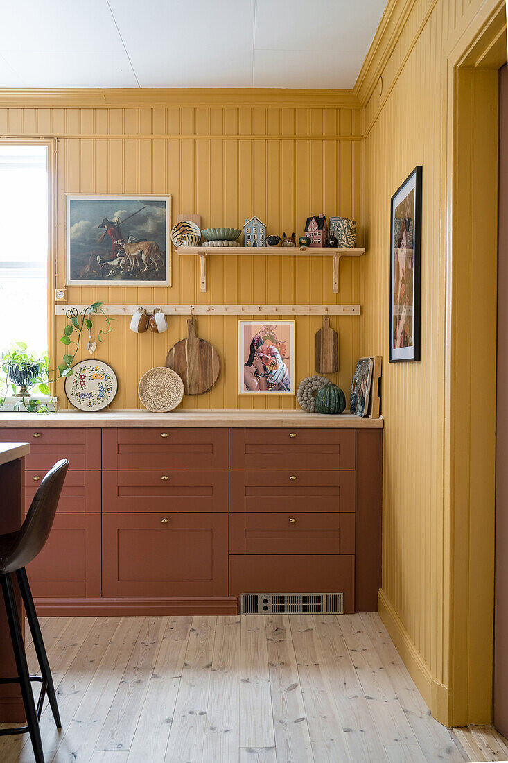 Kitchen with yellow wood paneling and terracotta-colored cupboards and decorative items