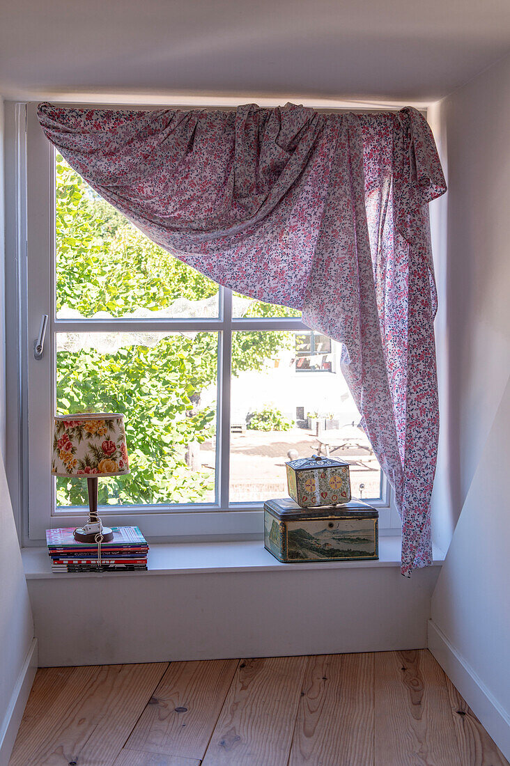 Window sill with floral curtain, lamp and vintage decorative boxes