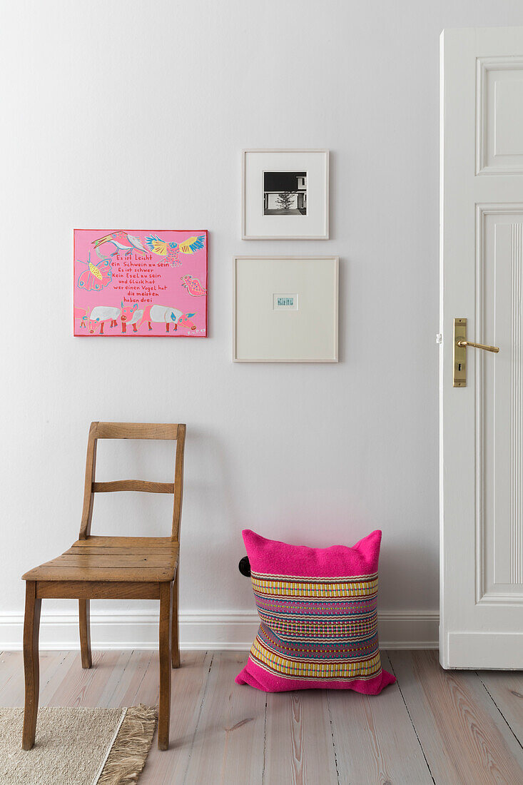 Wooden chair and pink pillow in front of a white wall with artwork