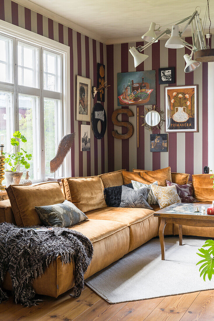 Living room with golden velvet corner sofa in front of purple and white striped wallpaper and gallery wall