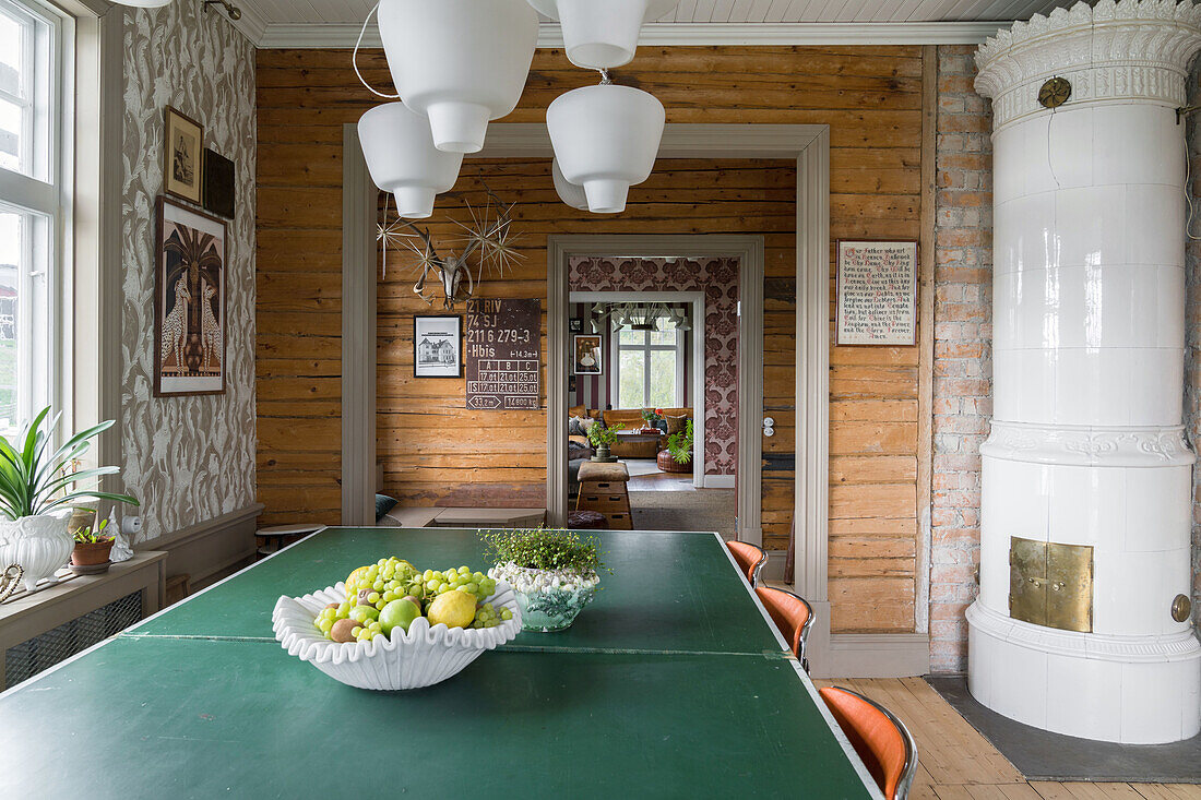 Esszimmer mit grünem Tisch, Holzverkleidung und traditionellem, weißen Kachelofen