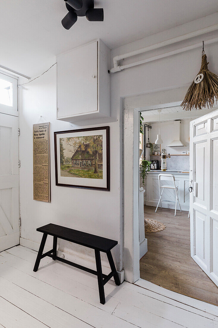 White hallway with black wooden bench and view into the kitchen