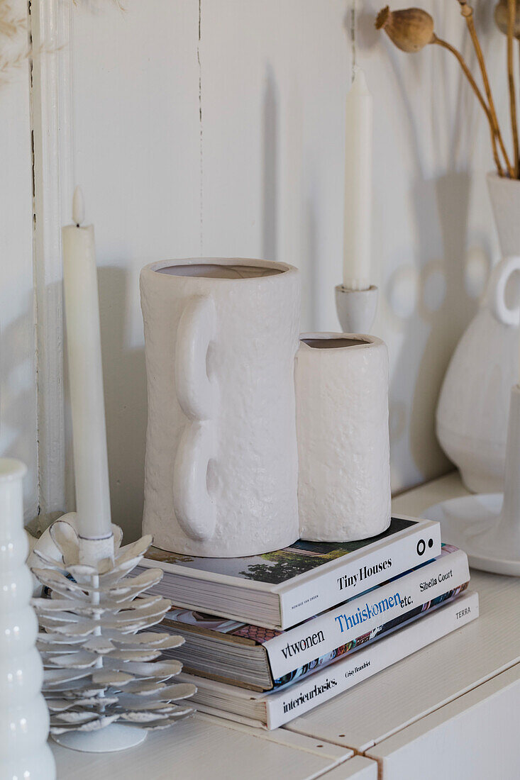 Sideboard with candlesticks and white vase on a stack of books