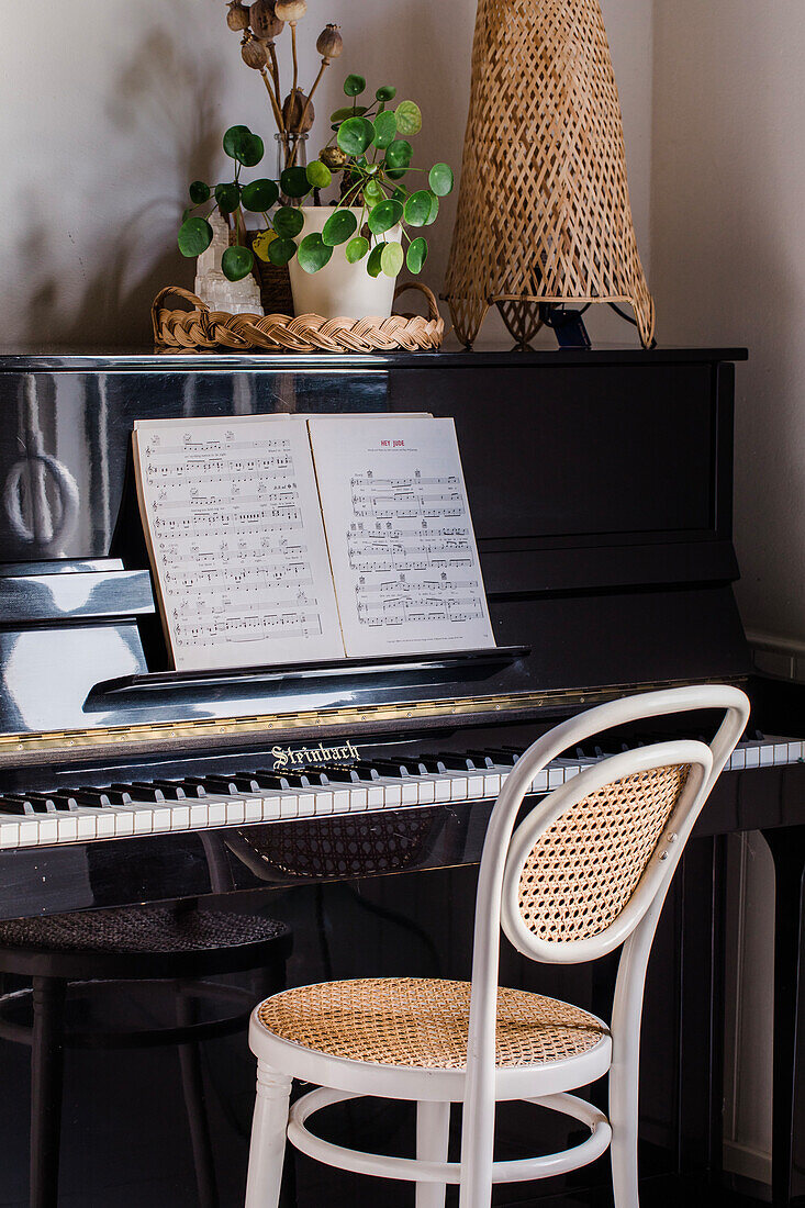 Black piano with sheet music, chair with Viennese wickerwork and houseplant