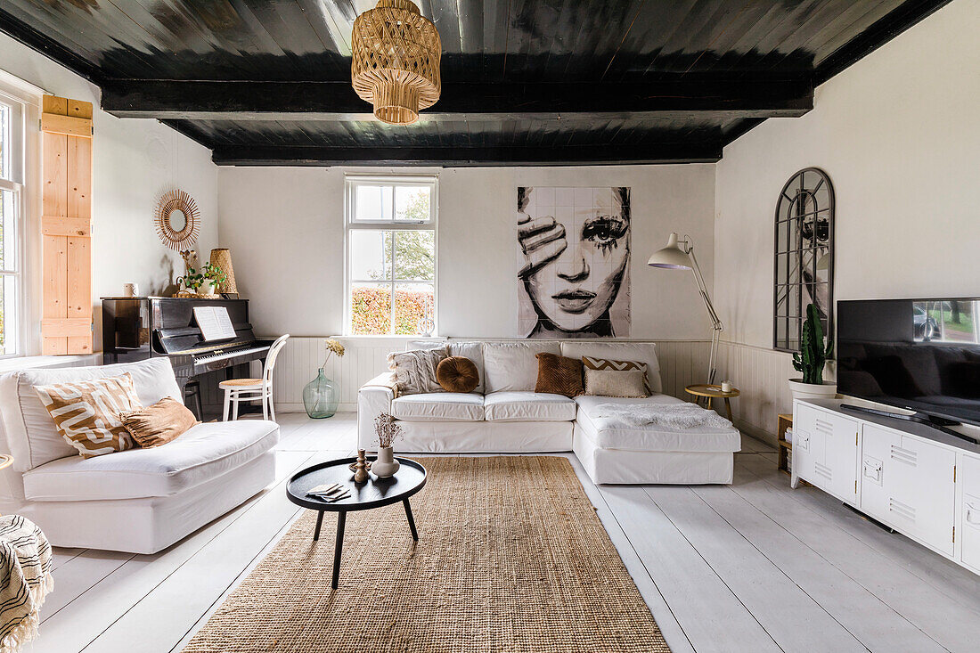 Living room with corner sofa and piano, black-painted wooden beamed ceiling