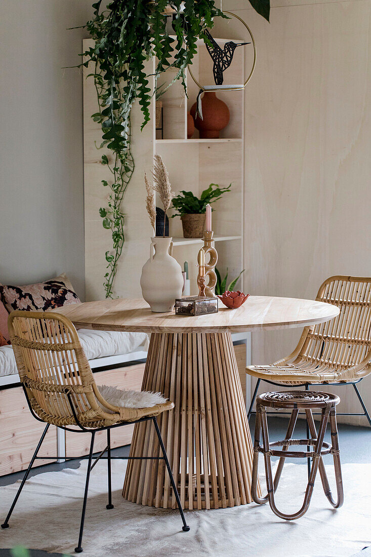 Modern, round wooden table with rattan chairs and hanging green plants on a wooden shelf