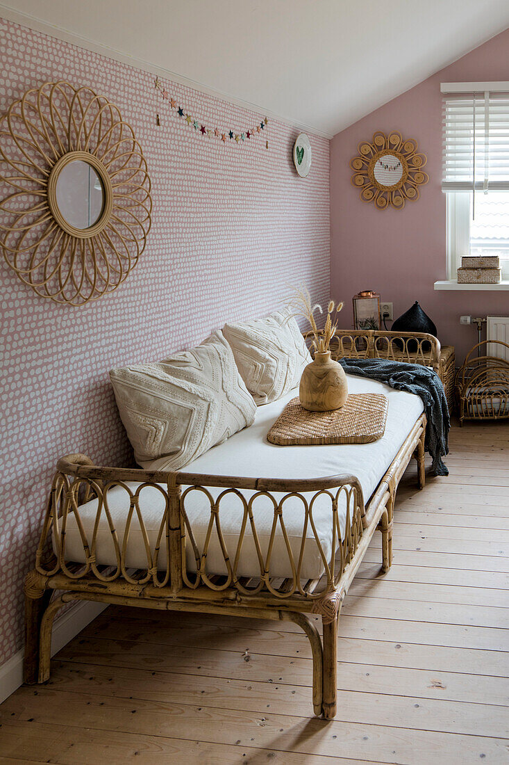 Rattansofa mit hellen Kissen und Wandspiegel an rosa Wand im Vintage-Stil