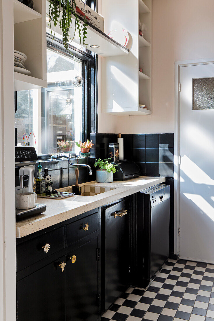 Bright kitchen with black cupboards and chequerboard pattern floor tiles