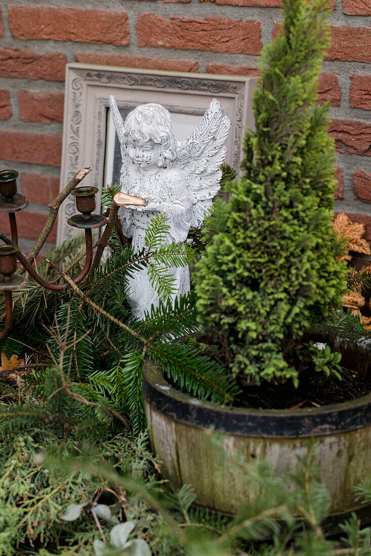 Engelsfigur neben Thuja im Holztopf mit Tannenzweigen und Kerzenhalter