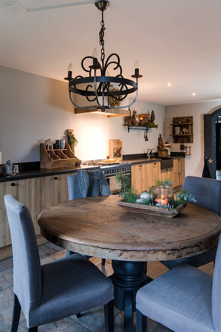 Round wooden table with grey chairs and antique chandelier in kitchen