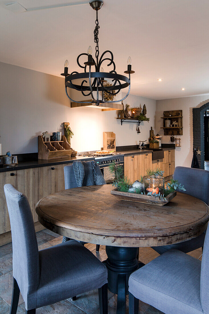Runder Holztisch mit grauen Stühlen und antikem Kronleuchter in Küche