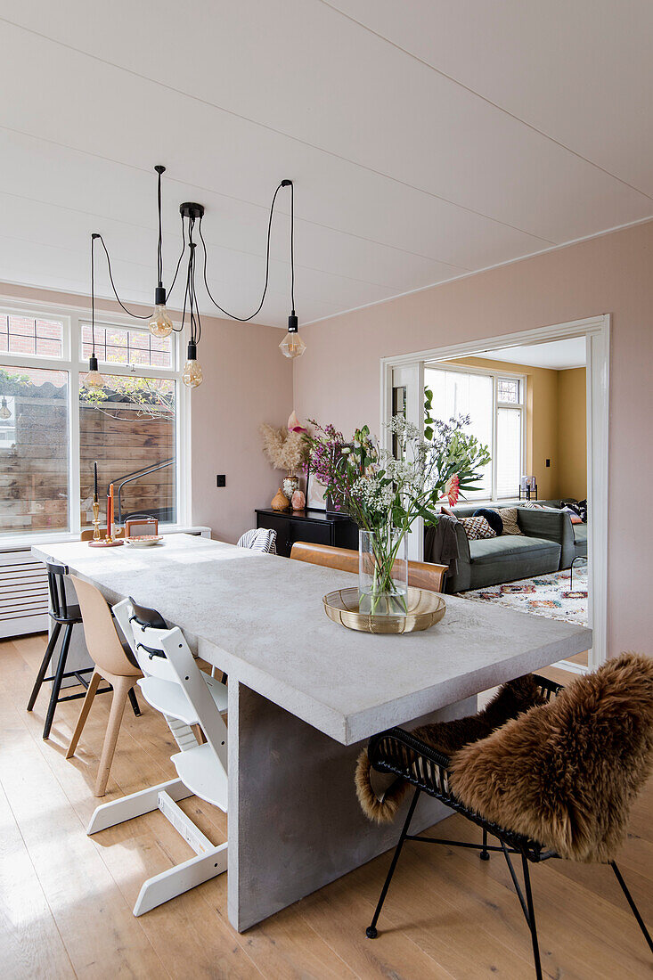 Dining table with concrete top, modern lighting and view into the living room