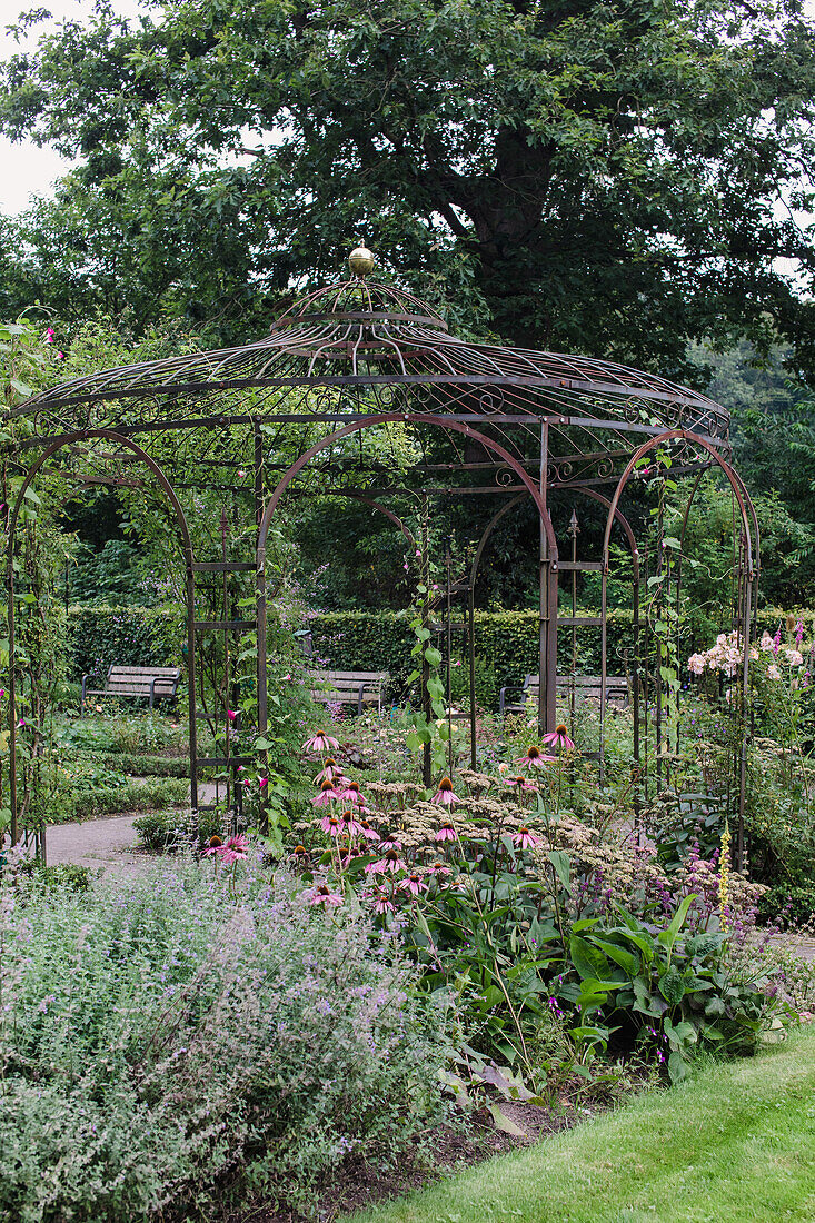 Pavillon aus Metall mit üppiger Begrünung und blühenden Stauden im Garten