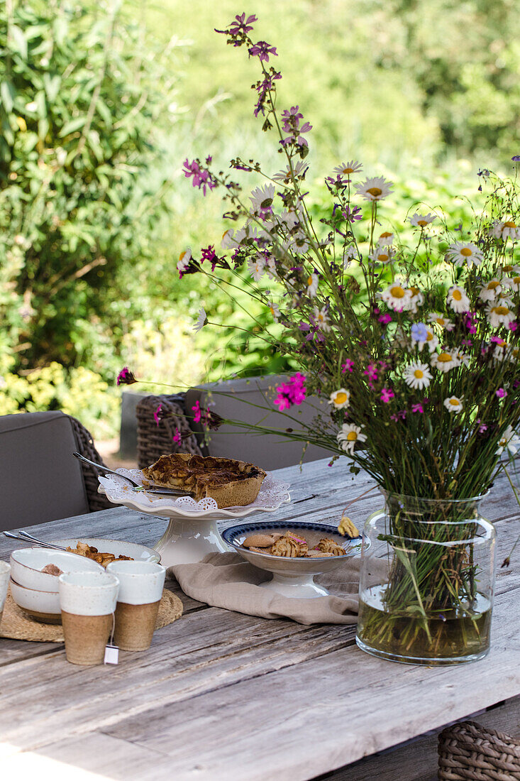 Sommerlicher Gartentisch mit Wildblumenstrauß und Gebäck