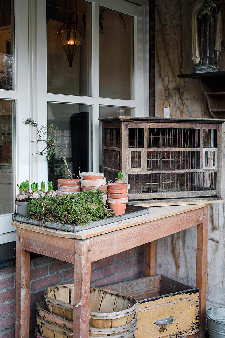 Rustikaler Gartentisch mit alten Tontöpfen und Pflanzen vor einem Fenster