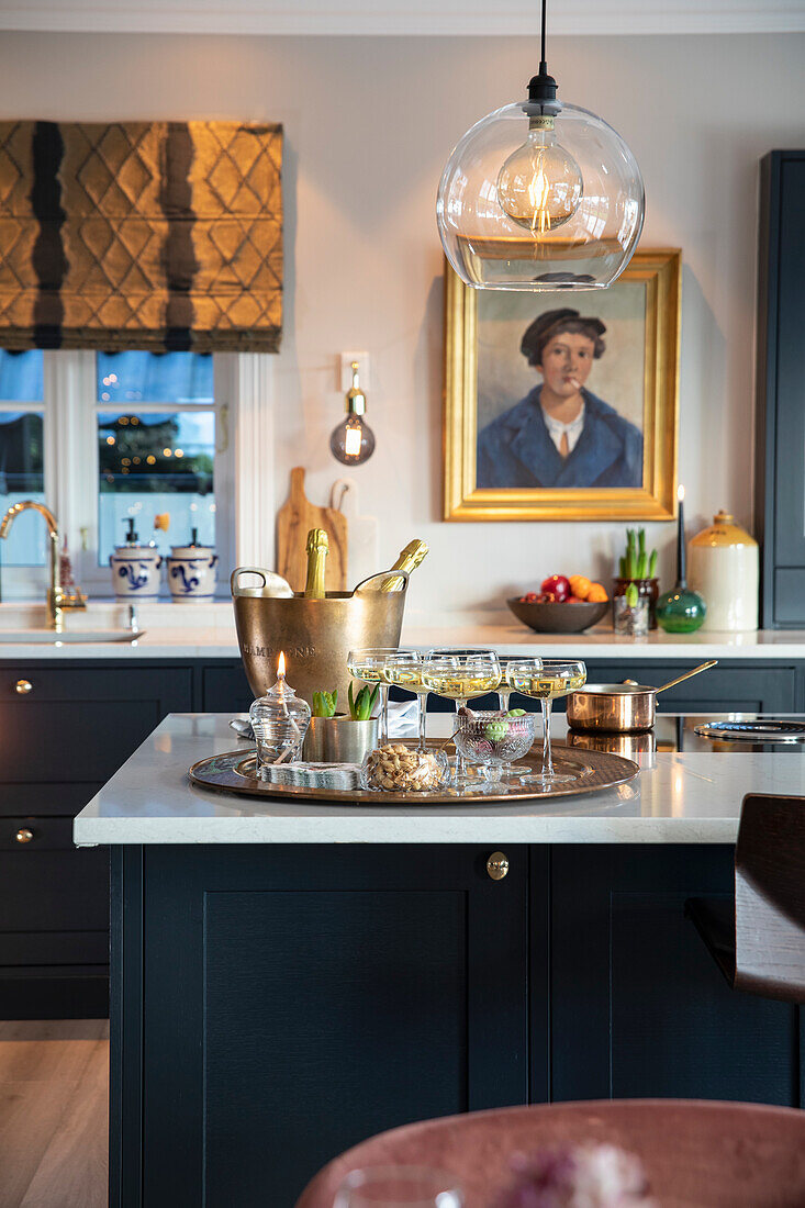 Kitchen island with champagne cooler, tray and glasses, hanging lamp, dark kitchen with white worktops