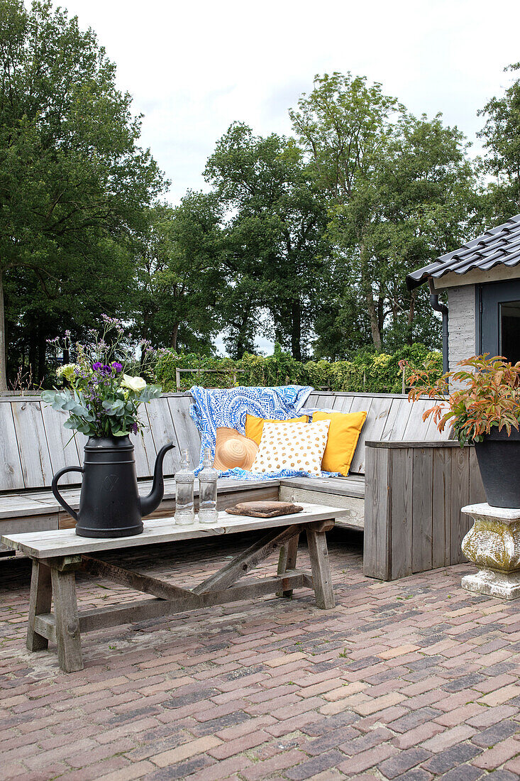 Rustikale Gartenterrasse mit Holzmöbeln und Blumenarrangement