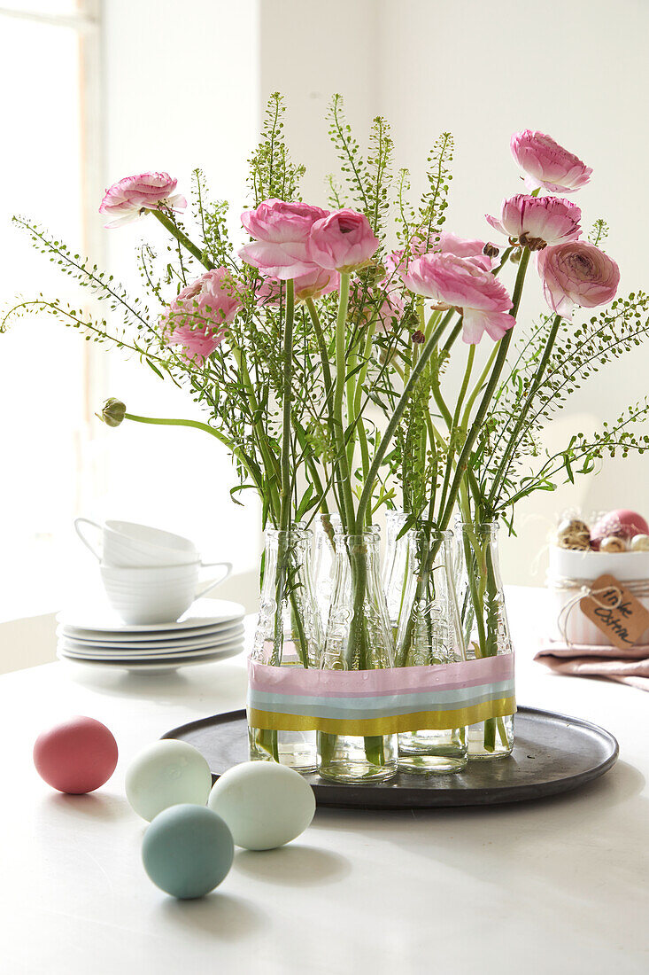 Pink-colored ranunculus in small glass vases on a tray