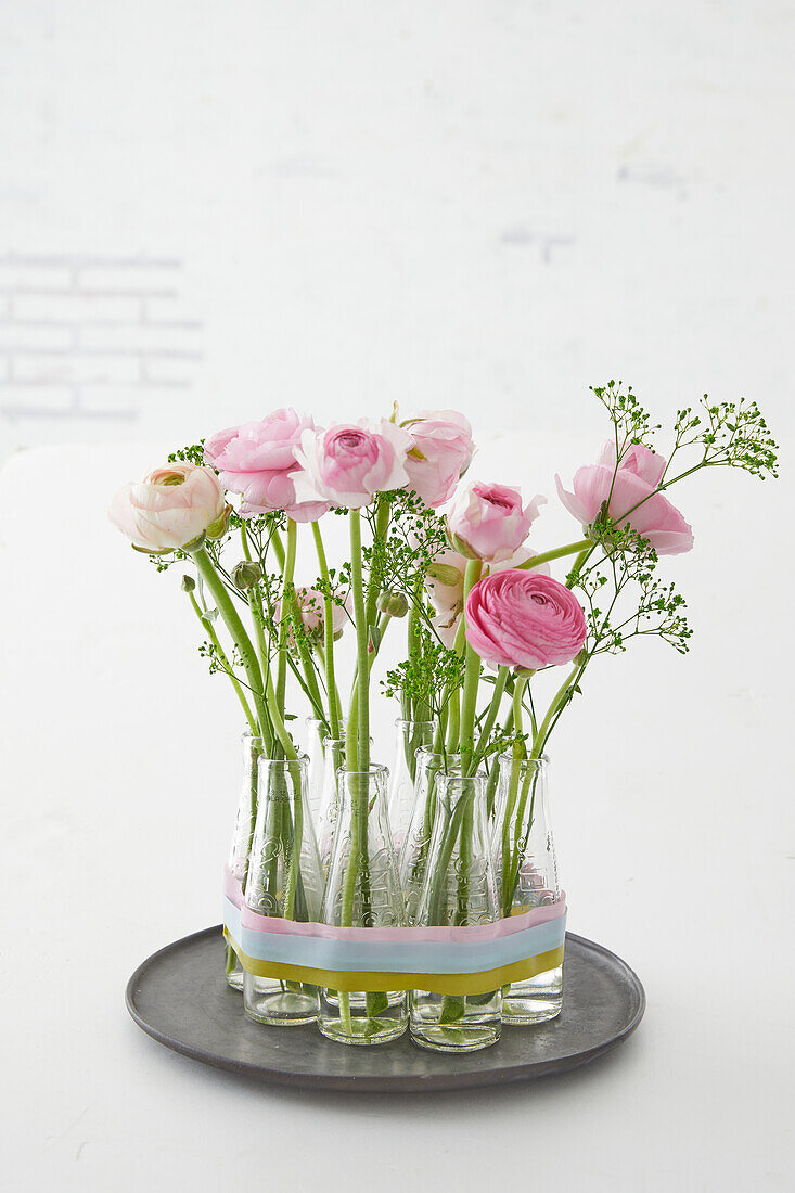 Pink ranunculus in small glass bottles on a metal tray