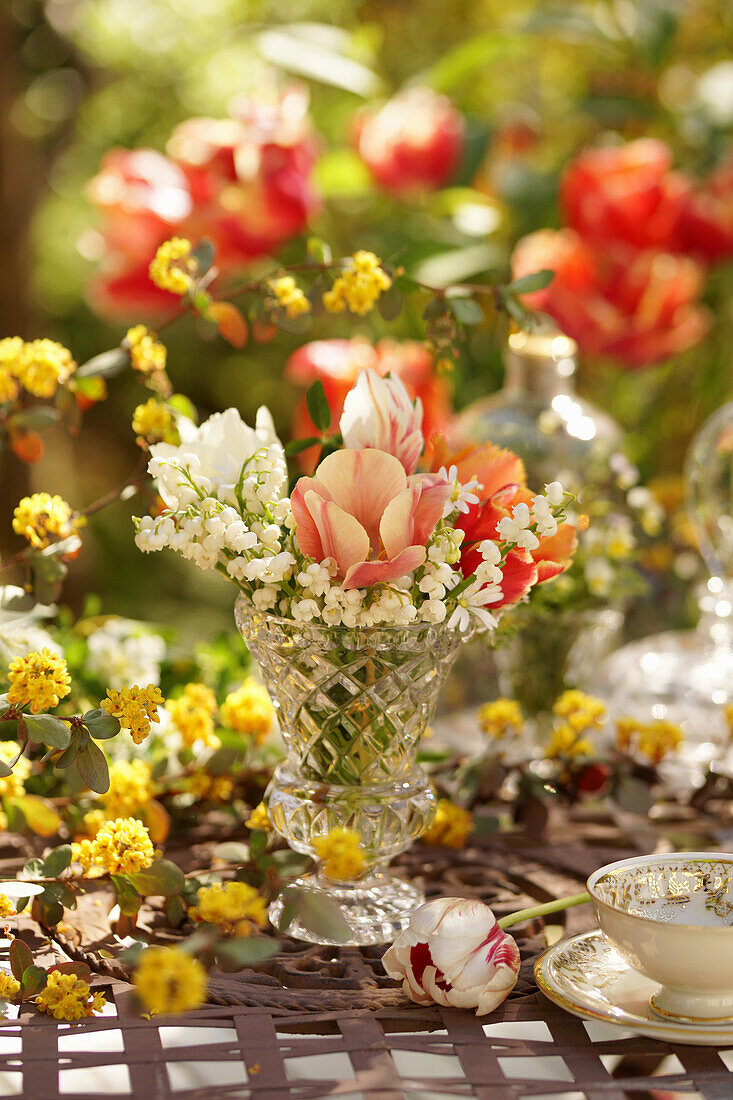 Blumenstrauß aus Tulpen (Tulipa) und Maiglöckchen (Convallaria) in Vase auf Gartentisch