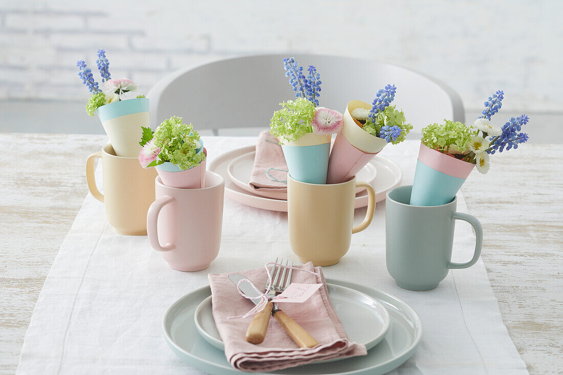 Frühlingshafte Tischdekoration mit Blumensträußen in pastellfarbenen Bechern