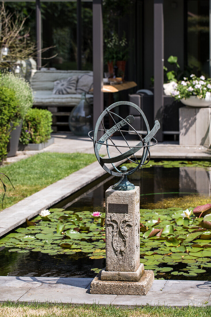 Garten mit Sonnenuhr-Skulptur und Seerosenteich vor moderner Terrasse