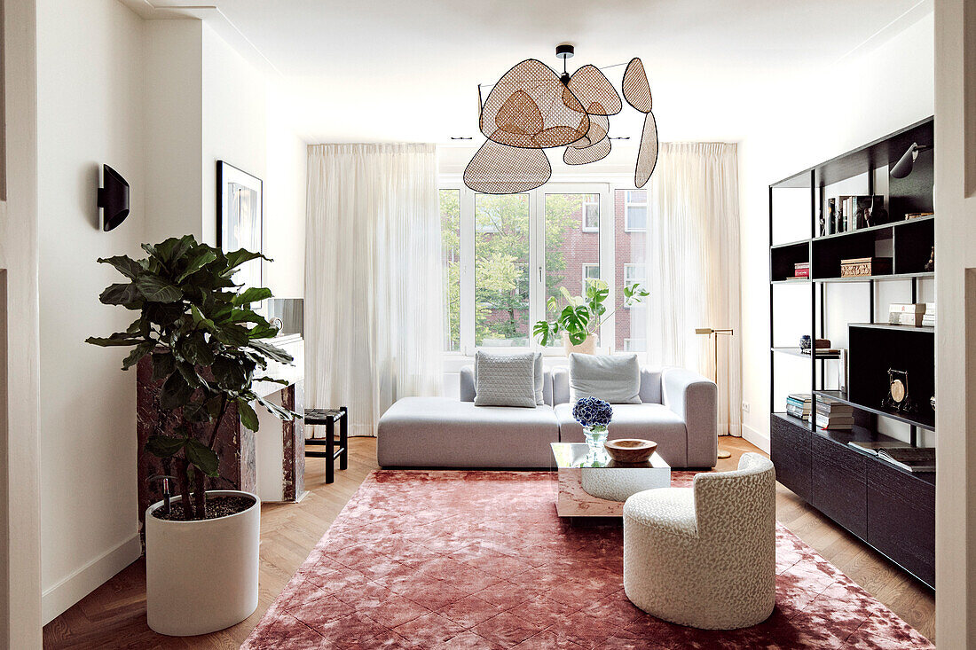 Modern eingerichtetes Wohnzimmer mit ausgefallener Hängeleuchte und rosa Teppich