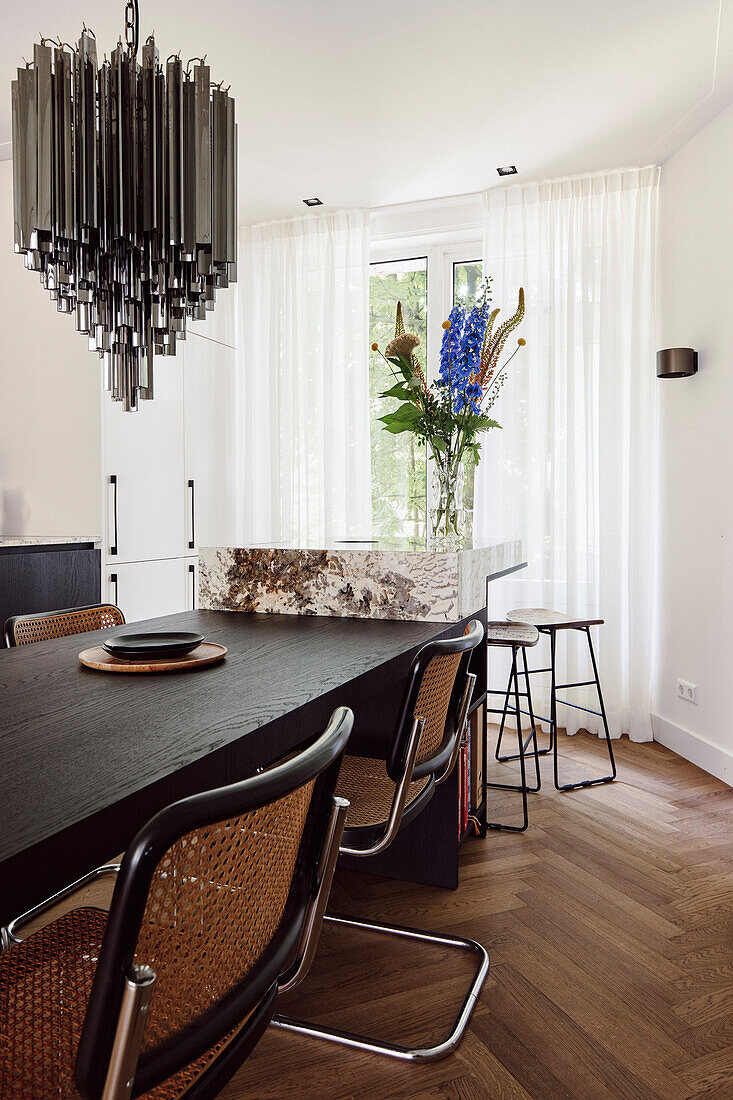 Esszimmer mit schwarzem Holztisch, Rattanstühlen und moderner Hängeleuchte