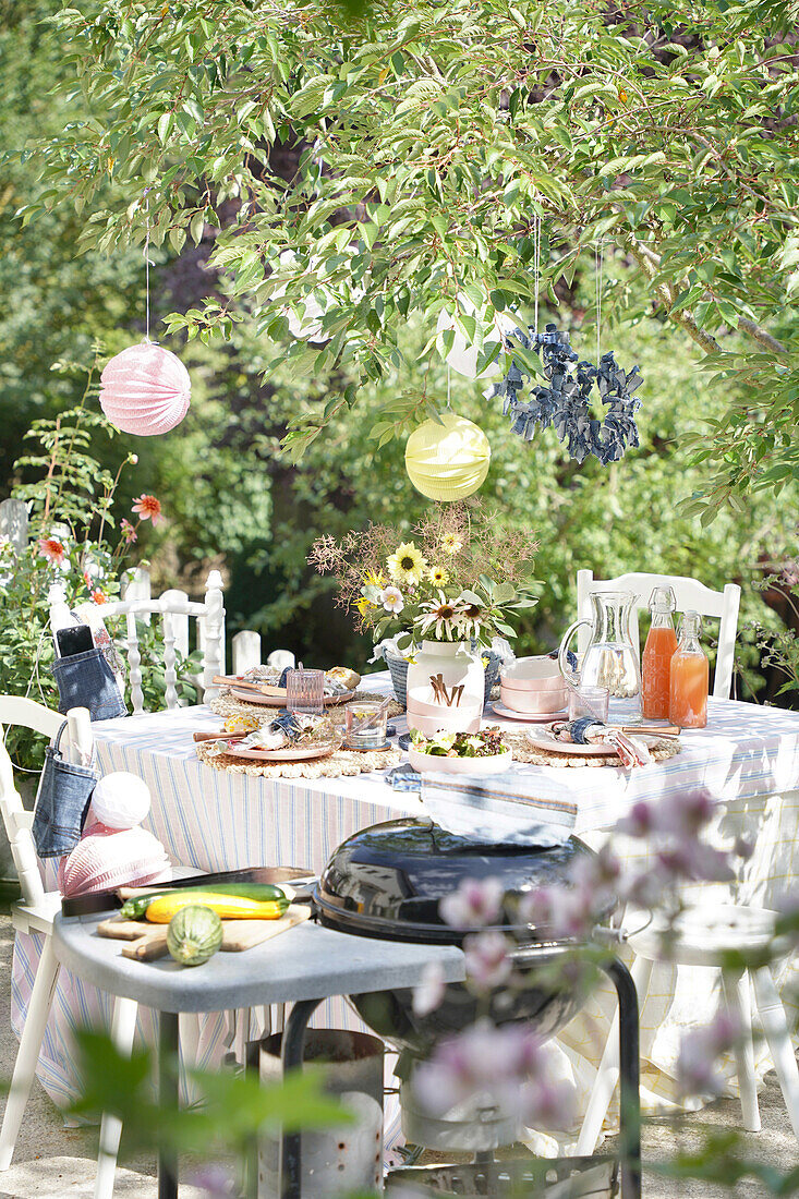 Summery garden table under trees with flowers and drinks