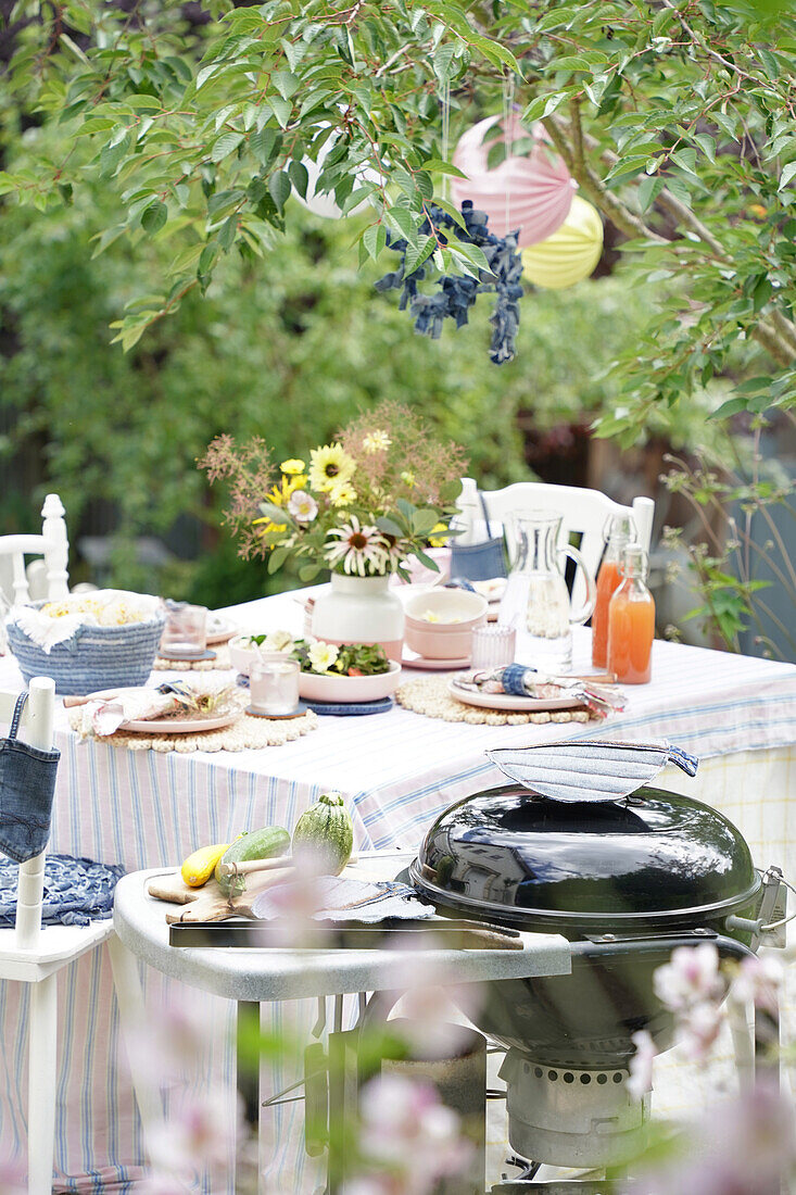 Laid garden table, barbecue and summery decoration in the countryside