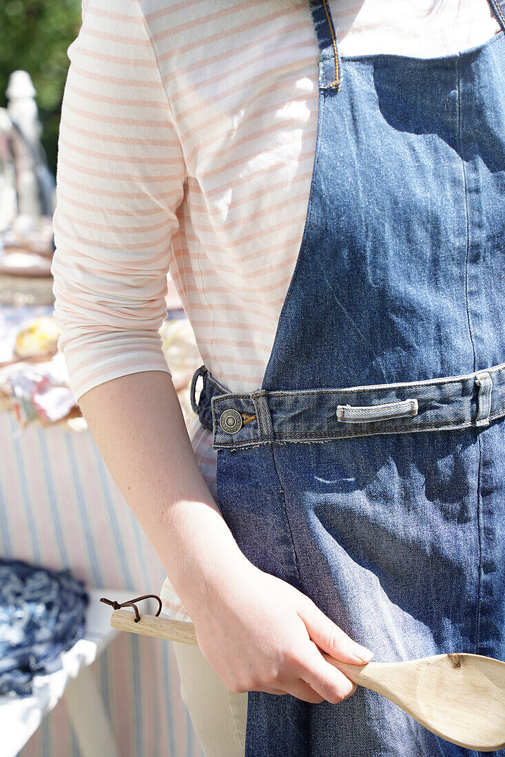 Person with denim apron and wooden spoon outdoors