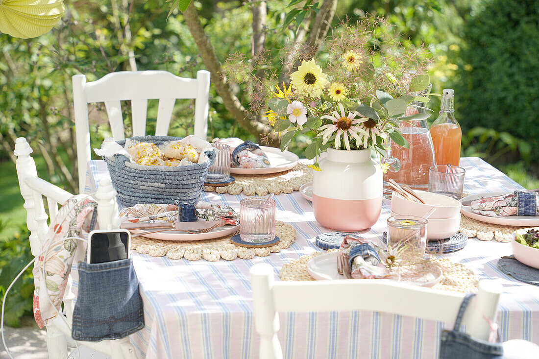 Sommerlich gedeckter Tisch im Garten mit Blumenstrauß und Brotkorb