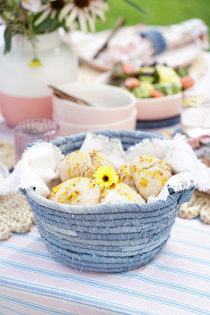 Home-baked bread rolls with flowers in a basket on a laid table in the garden