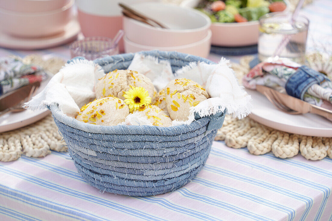 Denim bread basket with fresh bread rolls on an outdoor table setting