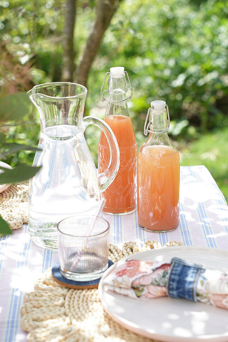 Sommerlicher Gartentisch mit Wasserkaraffe und Fruchtsaft in Bügelflaschen