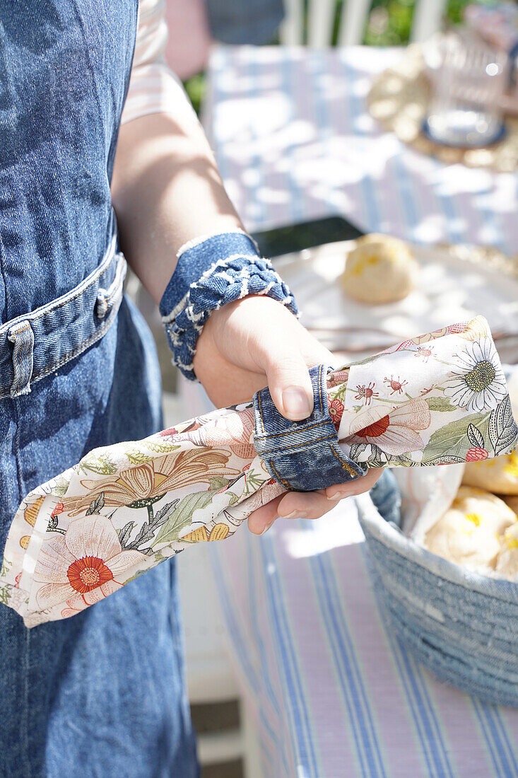 Hand holding napkin with floral pattern and denim napkin ring