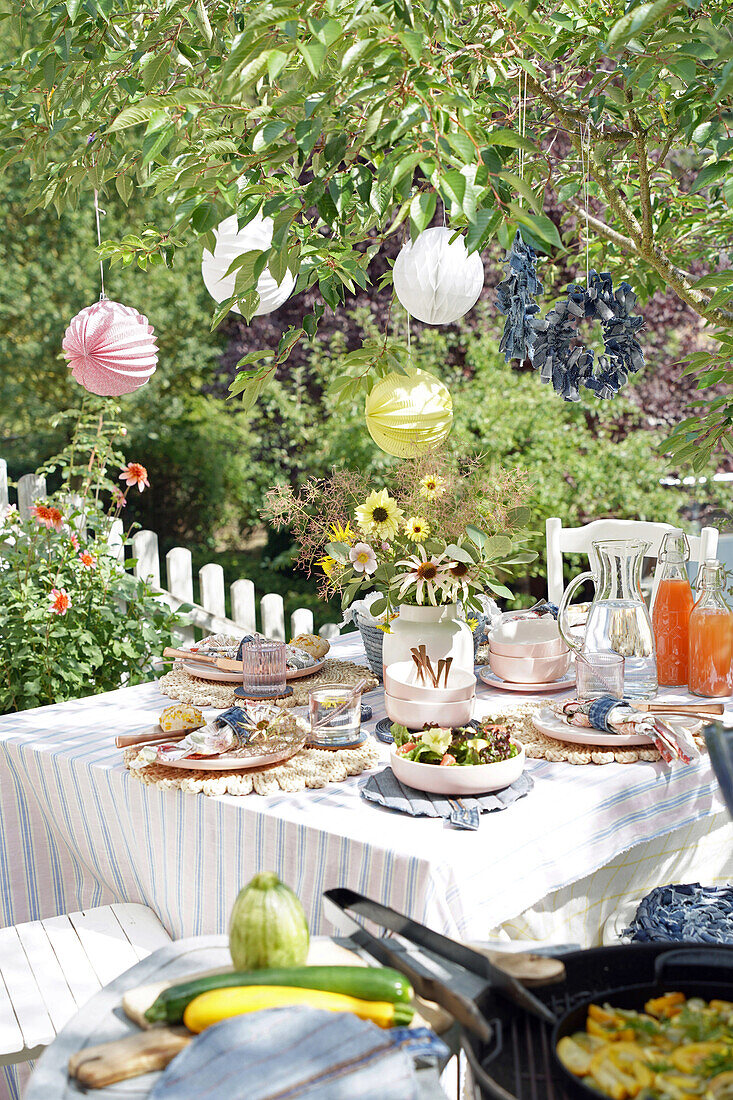 Summery table setting in the garden with bouquet of flowers, lanterns hanging in the tree