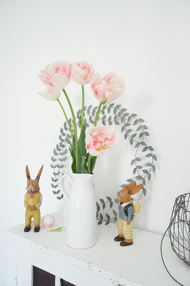 Old wooden cabinet with pastel pink tulip bouquet, wreath and Easter bunny figurines