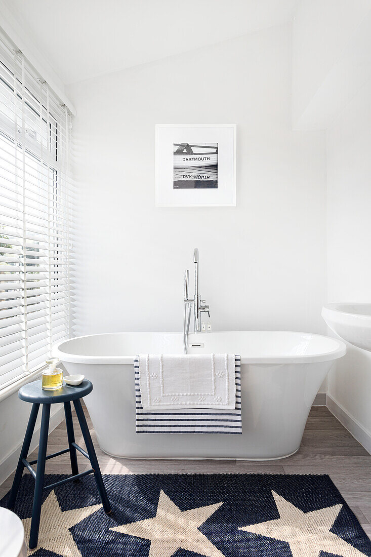 Freestanding bathtub with towels, starry carpet and stool in light-colored bathroom