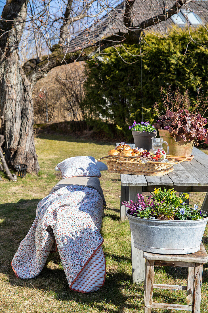 Spring picnic with tray on wooden table in the garden, blanket and cushion