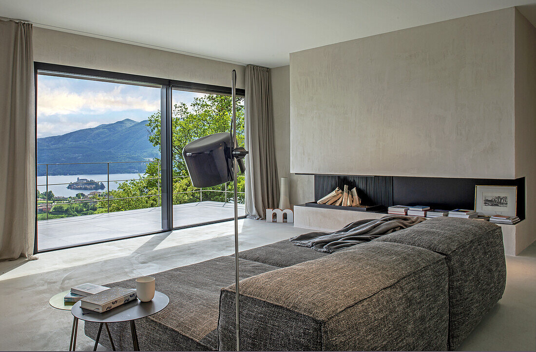 Wohnzimmer mit Panoramafenster und Blick auf Berge und See