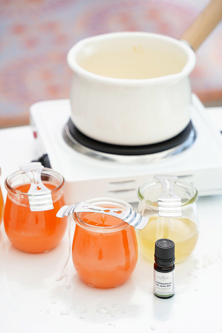 Candle making with colored wax in preserving jars and scented oil on a white table