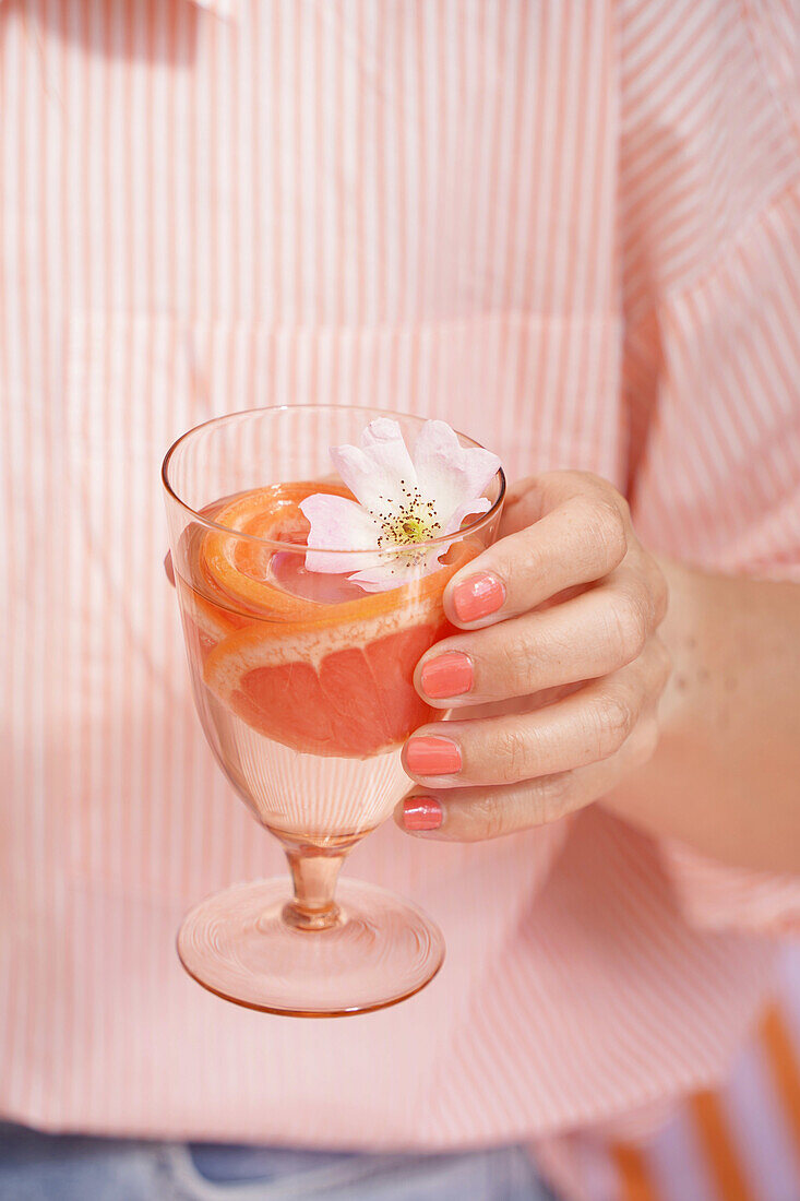 Glas mit Wasser und Grapefruitscheiben, dekoriert mit Blüte