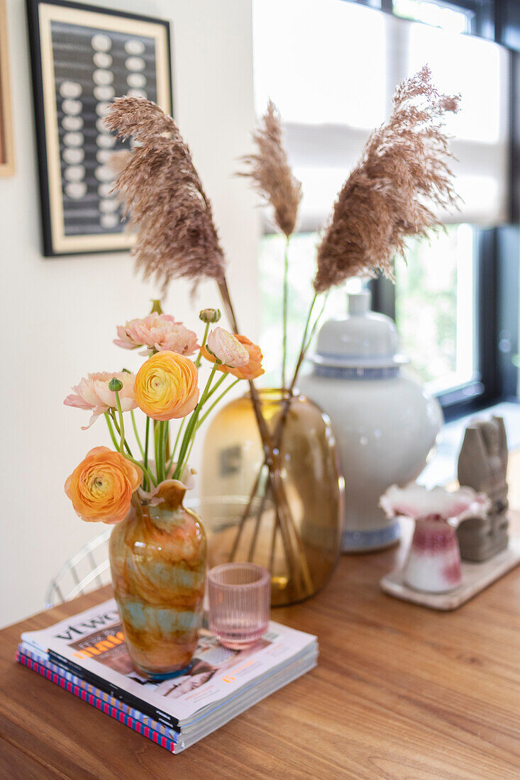 Vasen mit Ranunkeln (Ranunculus) und Pampasgras auf Holztisch