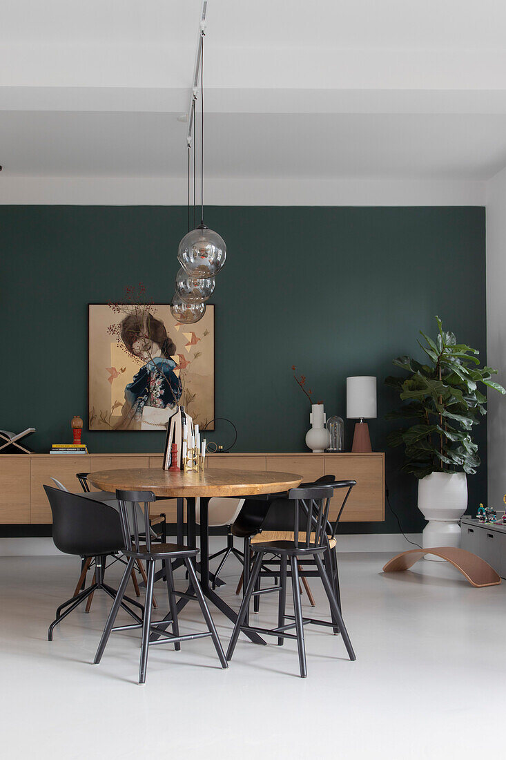 Round wooden table with black chairs in front of dark green wall in dining room