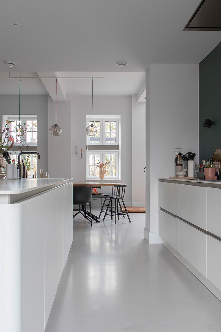 Modern white kitchen with cooking island and view into the dining room with black chairs